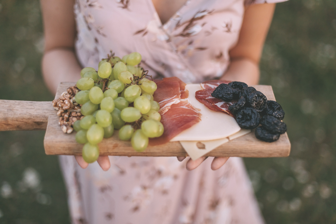 tray of deli meats, cheese and grapes hold by a woman